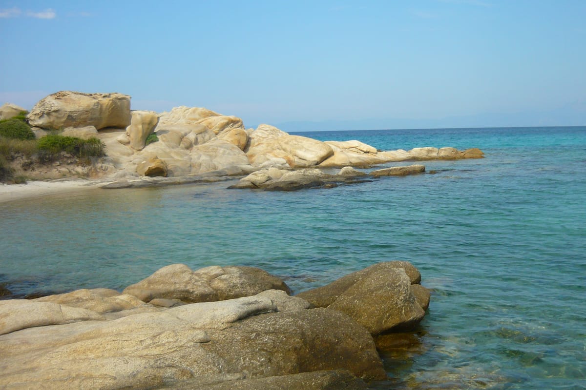 The sea pool of Karydi beach at Vourvourou, white rocks and shallow turquoise water, with the gulf of Mount Athos beyond