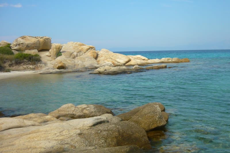 The sea pool of Karydi beach at Vourvourou, white rocks and shallow turquoise water, with the gulf of Mount Athos beyond