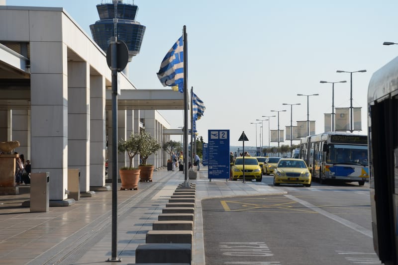 The kerb outside the main terminal of Athens International Airport: the colonnade, the control tower, taxis and the airport bus